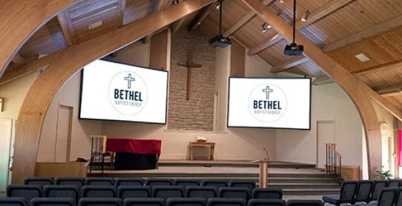 Short throw projectors illuminate two large screens above the pulpit of a church. Photo credit: Carl Lukings, Horizon Solutions