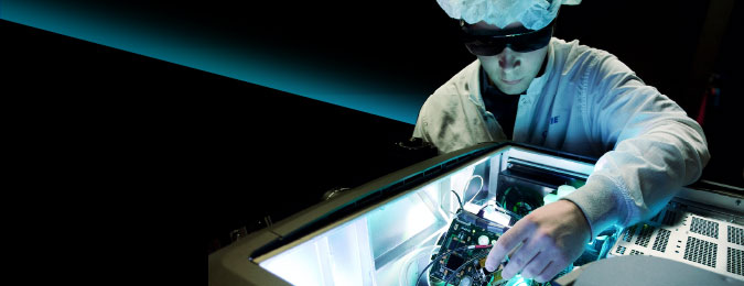 A technician in a white lab coat and hair net fixing a projector.