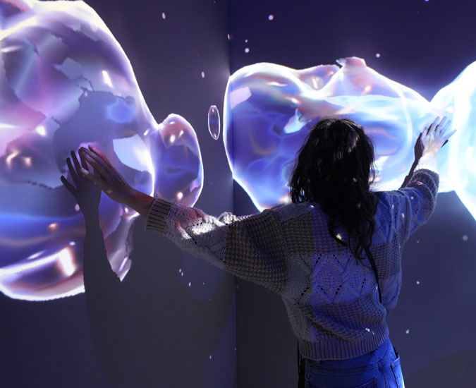 A person making the bubble images ona wall move with their hands, in Christie's immersive room at ISE 2025.