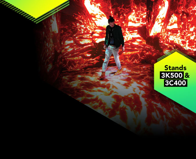 A perosn walking through a immersive room with flames projected onto the walls and floor.