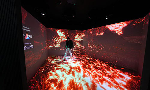 A person walking in an immersive room with projections of flames on the walls and floor.