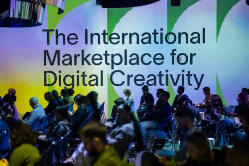 Group of people seated in rows with a floor-to-ceiling sign that reads 'the international marketplace for digital creativity' beside them.