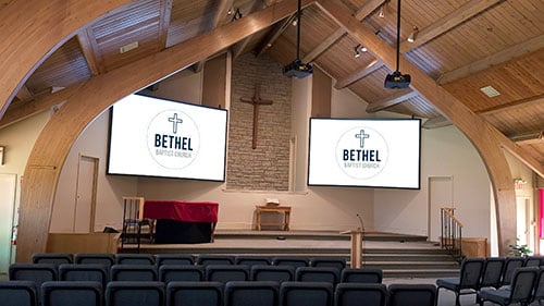 Projectors illuminate two large screens above the pulpit of a church.