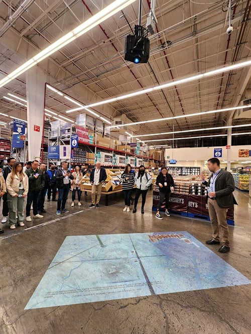 A group gathers around a projected image on the floor of a store.