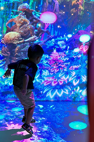 A small child plays in room with projection mapped walls and floor. 