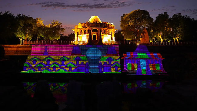 An intricate ancient temple is filled with colorful beams of light at night. 