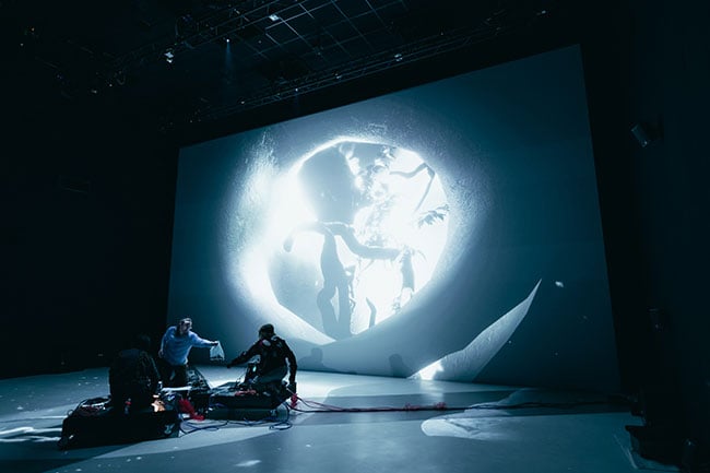 Several people interacting with projected images on a large screen and floor of an indoor theatre.