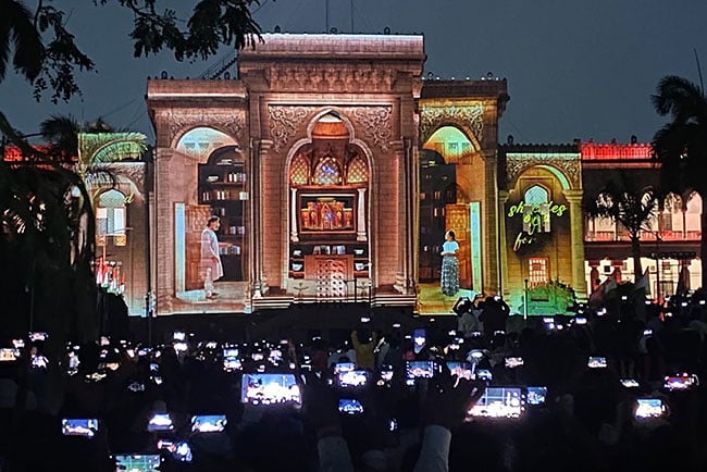 The façade of a large building is projection mapped in vibrant colors. 