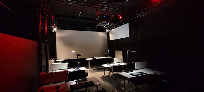 A darkened room with desks and a large screen at the front.