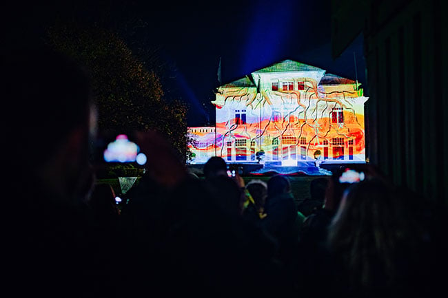 A two-story building is projection mapped in vivid colors.