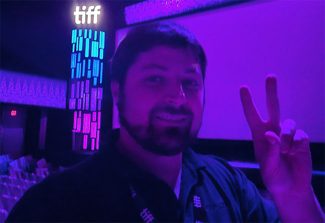 Close up of a man giving the peace sign in a darkened movie theatre.