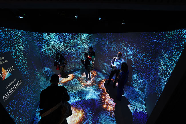 People explore a room with projected content on the walls and floor.