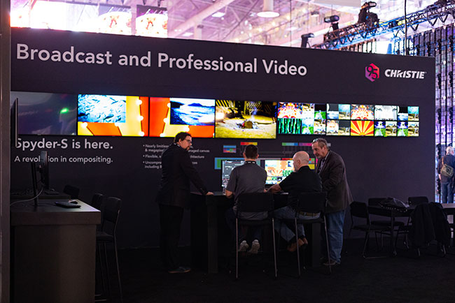 A group of people stand around a table on a trade show booth. 