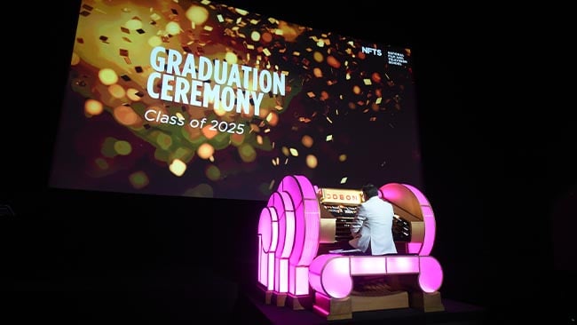 A person sits at an illuminated organ on a large stage.
