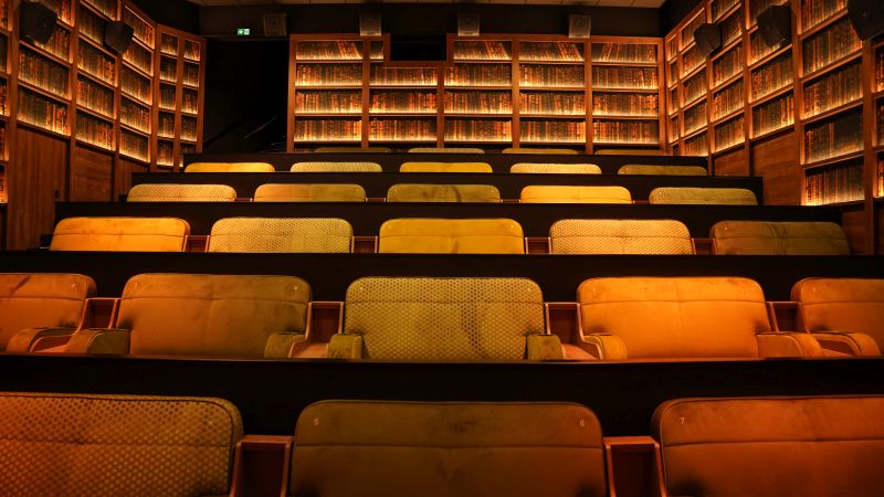A movie theatre with tan seats and walls lined with books.