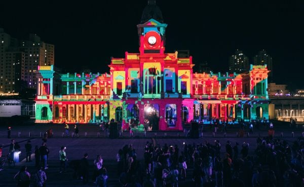 The façade of a large building is projection mapped with vibrant colors.
