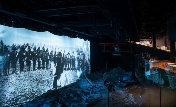 A large indoor screen shows a projected image of soldiers on a battlefield.
