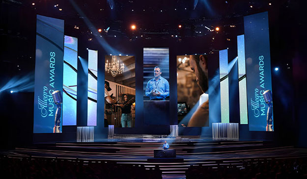 A person speaking on a large stage with vertical video walls surrounding them.