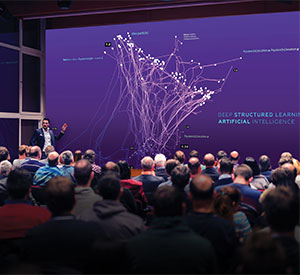 A person standing in front of a large Video Wall talking to an audience.