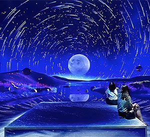 People sitting in a blue immersive room with a moon and swirling stars projected onto the walls and ceiling.