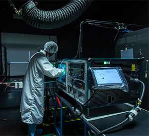 A technician in a white lab coat and hair net, repairing a projector